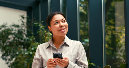 Happy Hispanic Business Woman Work Using Smartphone Phone. Motivation, Success at Office. Excited, Employee, Lawyer, Female Businesswoman Corporate Job. Greenhouse background