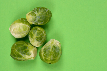 Five fresh Brussels sprouts are tightly grouped in the lower left corner against a bright, solid green background, creating a vibrant color contrast