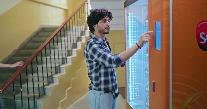 Indian happy young adult gen z smart male man use easy fast self service choose juice drink press button campus area. Lady female walk stairway thirsty boy take bottle enjoy break day time hallway