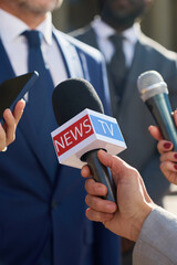 Caucasian middle aged man wearing suit speaking to journalists holding microphones during press...