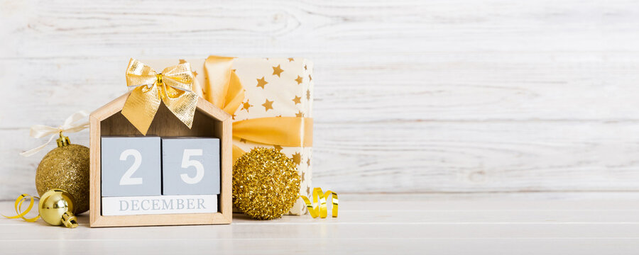 25 december. Christmas composition on colored background with a wooden calendar, with a gift box, toys, bauble copy space