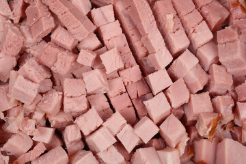 A close-up, high-angle view shows a large pile of uniformly diced pieces of cooked, pink ham or pork shoulder meat