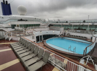 Guest pooldeck or swimmingpool with sun deck on modern family cruiseship or cruise ship liner with elegant lounge furniture deck chairs and rattan sun beds loungers after rain