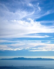 Vast, tranquil sky with wispy clouds,  a distant island, and a hazy horizon