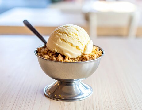 Creamy vanilla ice cream scoop atop a bed of crunchy granola in a metallic dish