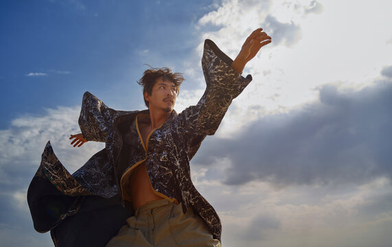 Man dancing outdoors in colorful chapan and kaftan under blue sky