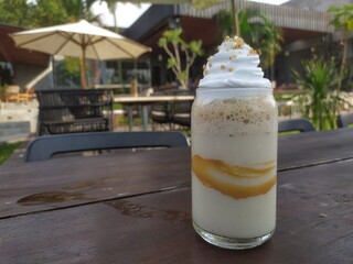 Creamy layered iced blended beverage topped with sweet whipped cream and golden sprinkles on a rustic wooden table in an outdoor cafe. Food concept