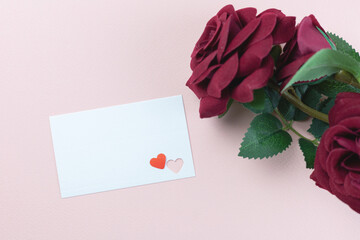 Top view, flat lay blank card with heart cutouts and deep red roses on pink background, perfect for love notes, romance, and special occasions.