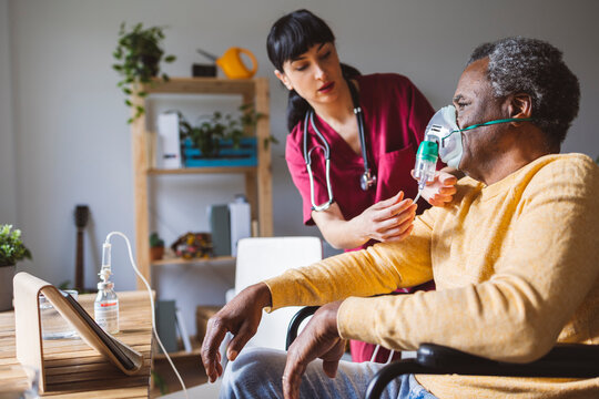 Caregiver putting oxygen mask on senior man sitting in wheelchair at home