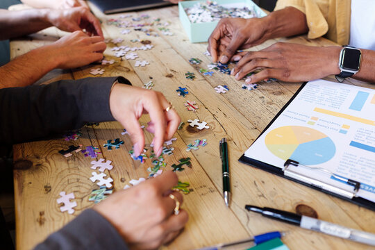 Hands of business colleagues playing jigsaw puzzle at workplace