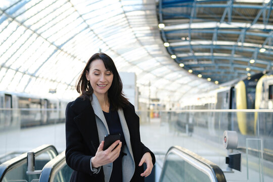 Happy mature woman using smart phone at railroad station