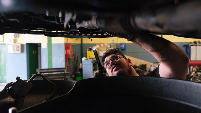 Mechanic using flashlight and inspecting lifted vehicle at workshop