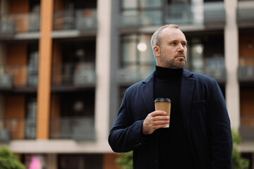 Adult man in elegant outfit holding coffee to go on street in autumn 