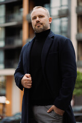 Adult confident man in coat looking at camera on city street