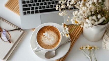 Cozy workspace with latte art coffee cup, laptop, flowers, and notebook for a creative and productive environment