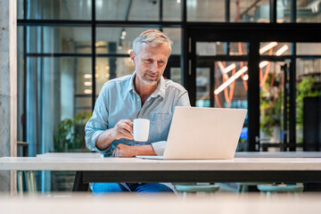 Businessman working with coffee in a modern office looking at laptop