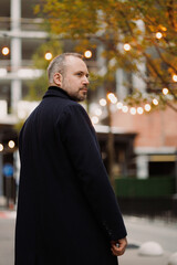 Bearded man in coat looking away on city street in autumn