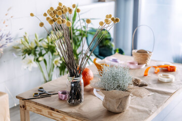 Decorative floral table with natural materials, pumpkins, and rustic arrangements in a small business workshop. Thanksgiving promo content, handcrafted branding, seasonal styling
