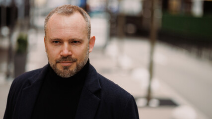 Portrait of adult man in coat standing on city street