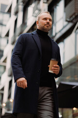 Portrait of elegant man in coat holding coffee to go on city street