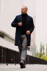 Full length of elegant man in coat walking on urban street
