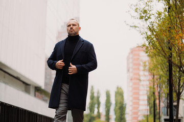 Adult man in elegant outfit and coat walking on city street