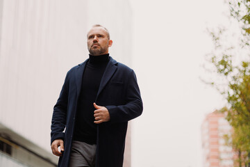 Elegant man in coat and turtleneck walking on city street
