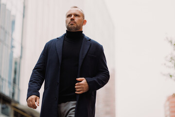 Confident businessman in coat walking on urban street in autumn 