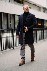 Elegant businessman in coat walking on city street in autumn