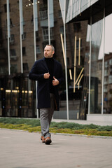 Full length of businessman in coat walking near office building on street