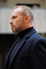 Portrait of adult businessman in coat standing on urban street