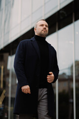 Businessman in coat and turtleneck walking near office building on street