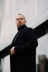 Confident man in turtleneck and coat standing near office on city street