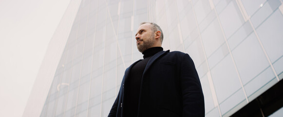 Low angle view of adult businessman in coat standing near office building, banner