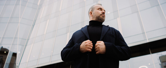 Low angle view of businessman wearing coat near office building on street, banner