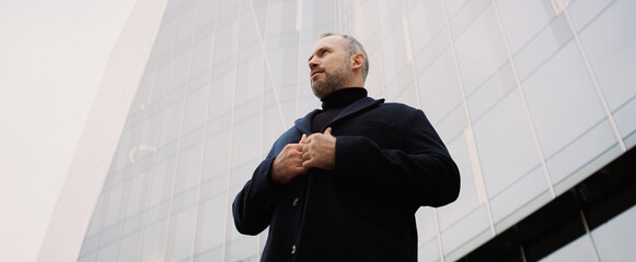 Businessman wearing coat near high-rise building on street, banner
