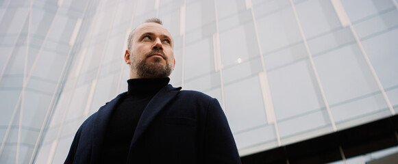 Portrait of businessman standing near high-rise building on street, banner