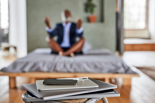 Gadgets on table with businessman meditating on bed at home