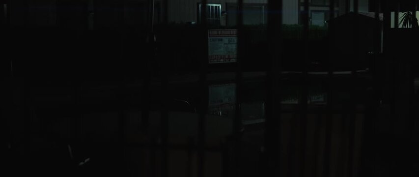 Dark night swimming pool behind fence with caution sign and reflections in the water