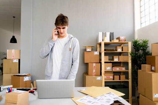 Businessman talking on mobile phone while working on laptop at office