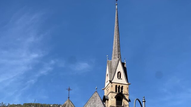 Historic church tower in Moena, Italy, standing under a clear blue sky with the Dolomite mountains in the background - a perfect example of alpine architecture and serene village charm.