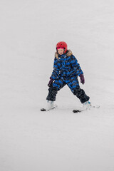 Child learning to ski during a snowfall in the mountains. A winter sports scene capturing the joy...