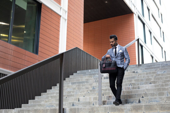Businessman checking time and moving down on staircase outside office building