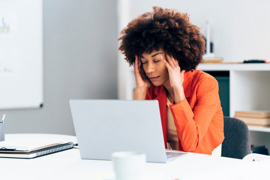 Businesswoman with head in hands sitting with laptop at desk in office