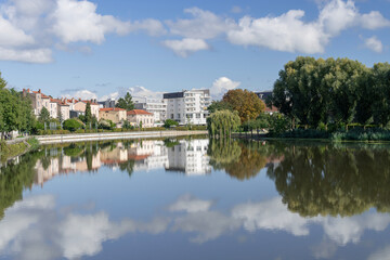 Fototapeta premium Saint-Max, France - September 27th 2025 : View of the banks of the La Meurthe river at Saint-Max with modern buildings, trees and reflections on the water.