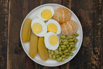 A plate of healthy breakfast. Balance diet. Boiled egg, steamed banana, boiled edamame, tangerine.