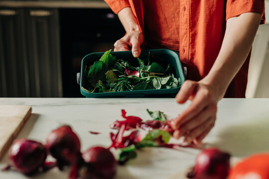 Person collecting vegetable scraps for compost in kitchen