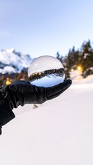 Hand holds crystal ball reflecting snowy mountain scene