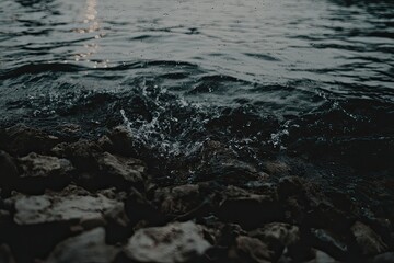 Dark water laps rocky shore, glimmering light reflecting on the surface