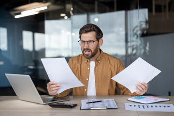 Frustrated entrepreneur in modern office clutching financial reports and calculator, staring at laptop in distress over budgets, taxes and paperwork under looming deadline